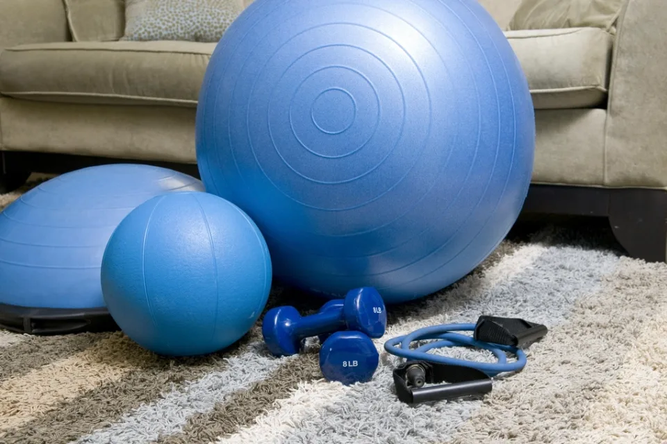 Bola de exercício, halteres e elástico no tapete da sala