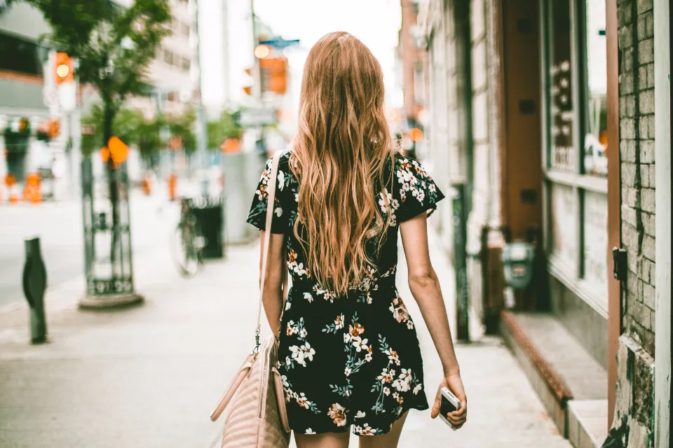 Mulher caminhando por uma rua arborizada da cidade