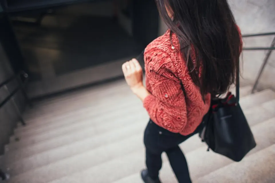 Mulher de blusa vermelha subindo uma escada, vista de costas